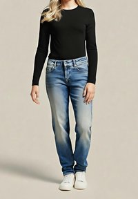 Jeans blu sbiaditi a taglio dritto, abbinati a una maglia nera a maniche lunghe. Scarpe da ginnastica bianche completano il look, enfatizzando uno stile casual.