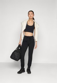 Fekete sportos tréningnadrág, állítható derékkal, fekete crop top-pal és fehér cropped dzsekivel párosítva, fekete edzőtáskával a kezében.