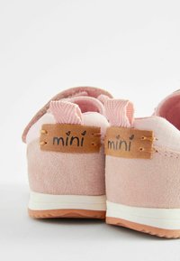 Rosa mockaskor med en texturerad överdel, kontrasterande gummisula och en läderetikett med "mini" i svarta bokstäver.