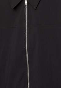 Schwarzes Zip-Up-Shirt mit Kragen, das einen silbernen Reißverschluss auf der Vorderseite sowie eine glatte, leichte Stofftextur aufweist.