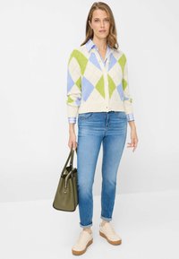 Pull : crème avec motif losanges verts et bleus, manches longues, boutonné devant. Jean : bleu clair, coupe slim. Accessoires : sac à main olive, baskets beiges.