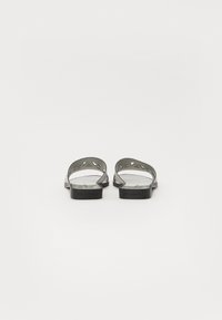 Sandalias negras con una parte trasera abierta, que presentan un diseño recortado en las correas. Material suave con una suela plana y un tacón mínimo.