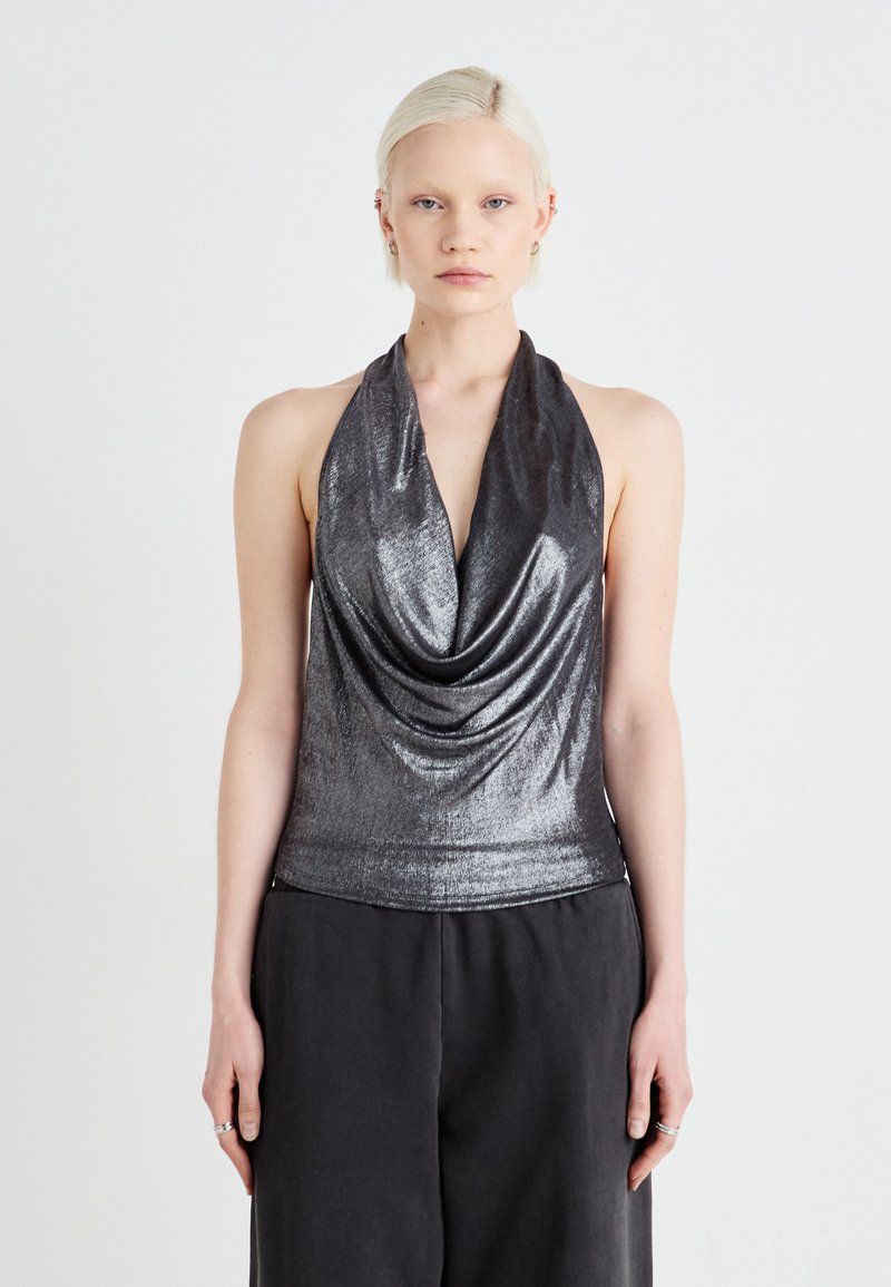 Metalni srebrni halter top s drapiranim izrezom, uskim dizajnom, glatkom teksturom i minimalističkim stilom, uparen s tamnim širokim hlačama.