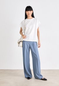 T-shirt bianco a maniche corte, pantaloni ampi blu chiaro, scarpe basse nere e una piccola borsa color crema con dettagli dorati. Design minimalista, texture liscia.