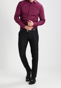 Chemise bordeaux à manches longues avec fermeture par boutons, associée à un pantalon noir sur mesure et des chaussures noires. Tissu lisse avec une coupe ajustée.