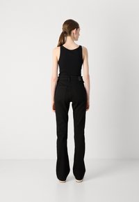 Pantalons évasés noirs avec taille haute, forme structurée et deux poches arrière. Associés à un débardeur noir ajusté.