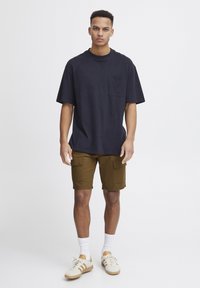Marineblå bomulds T-shirt med brystlomme, parret med olivengrønne cargo shorts med sidelommer, hvide ankelsokker og hvide sneakers med accenter.
