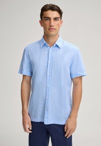 Lichtblauwe kortelange knopsluiting shirt van gestructureerde stof. Heeft een standaard kraag en zeven knopen aan de voorkant.