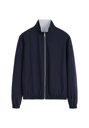 Veste zippée bleu marine avec un col haut, des poignets et une taille élastiques. Comprend deux poches latérales et un tissu lisse et léger.