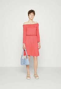 Vestido coral ombro a ombro com uma cintura ajustada e saia rodada. Combinado com uma bolsa azul clara e sandálias de plataforma brancas com alças verdes.