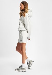 Grå hettegenser med kengurulomme og matchende grå shorts. Modellen har på seg grå sneakers med hvite sokker. Begge plaggene har en avslappet passform.