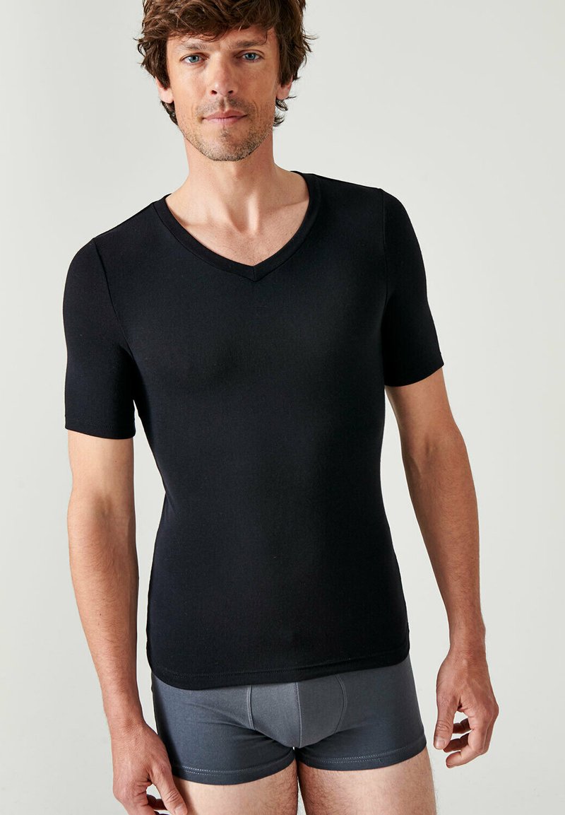 T-shirt nera a maniche corte con scollo a V, realizzata in un materiale elastico, design aderente, texture liscia, indossata con boxer grigi.