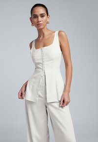 Wit linnen top met een vierkante halslijn, knopen aan de voorkant en een uitlopende peplum-silhouet, gecombineerd met bijpassende wijde linnen broek.