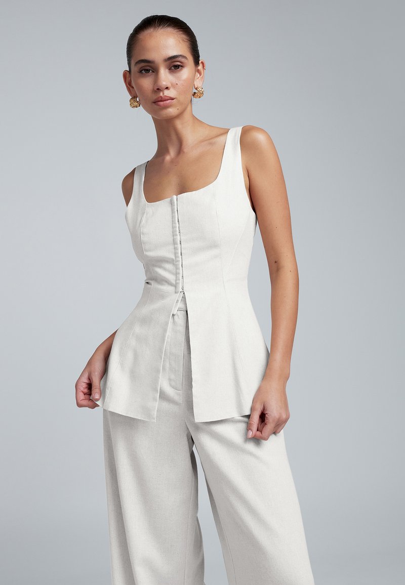 Wit linnen top met een vierkante halslijn, knopen aan de voorkant en een uitlopende peplum-silhouet, gecombineerd met bijpassende wijde linnen broek.