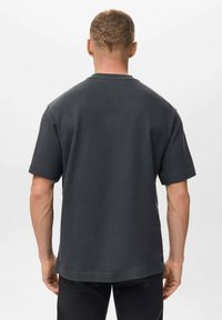 Tmavě šedé tričko s krátkým rukávem vyrobené z bavlny, s uvolněným střihem a hladkou texturou. Žádné viditelné vzory nebo akcenty.