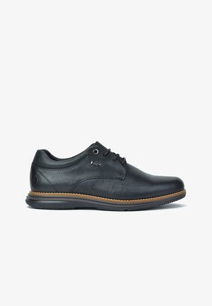 Zapato de vestir de cuero negro con punta redondeada, diseño con cordones y textura suave. Presenta una suela de goma marrón claro y un sutil detalle de logo.