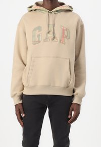 Beżowa bluza z kapturem z logo "GAP" w kolorowych blokowych literach, wyposażona w kaptur ze sznurkiem i kieszeń kangur, wykonana z miękkiej bawełnianej dzianiny mieszanej.