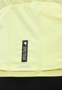 Ανοιχτό κίτρινο ύφασμα με κάθετη ραφή και μαύρη ετικέτα που αναγράφει "Authentic Endura Gear Designed in Scotland Made in UK".