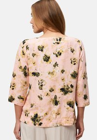 Blusa floreale rosa, realizzata in un tessuto morbido con motivi di fiori gialli e neri, maniche a tre quarti e vestibilità comoda.