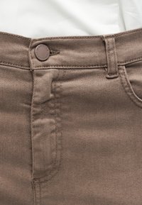 Καφέ τζιν από denim με μέση που έχει μεταλλικό κουμπί χαραγμένο με τη λέξη "Marella", θηλιά για ζώνη και ραφές μπροστινής τσέπης, εμφανείς πάνω σε λευκό ύφασμα.