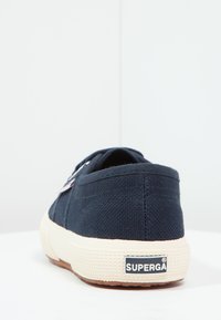 Marineblå kanvas sneakers med en teksturert overflate, gummisåle og kontrastfarget kremfarget mellomsåle. Har en logo på hælen og tradisjonell snøring.