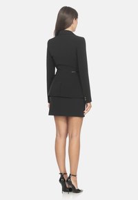 Blazer nero sartoriale con silhouette strutturata, abbinato a una gonna corta. Presenta maniche lunghe, design peplo e dettagli con bottoni dorati.