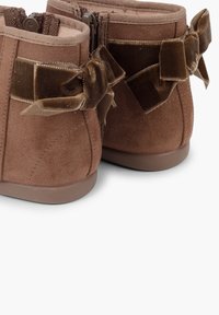 Braune Wildleder-Stiefeletten mit glatter Oberfläche, ausgestattet mit zwei dunkelbraunen Samtbows auf der Rückseite und einer Gummisohle für besseren Halt.