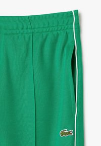 Grønne sports shorts lavet af åndbart stof, med hvid pipingside og et broderet krokodillelogo nær taljen.