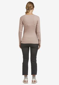 Langärmliges, tailliertes Oberteil aus weichem, rosa Rippstoff mit einem gewellten Ausschnitt und einer glatten Textur, kombiniert mit dunkelblauen, cropped Jeans und Sneakers.