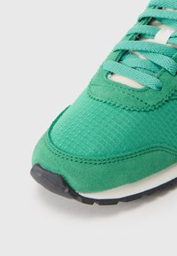 Grønn sneaker med en kombinasjon av teksturert stoff og semsket skinn, med flate snører og såle i svart gummi. Rund tå med stikkedetalj.