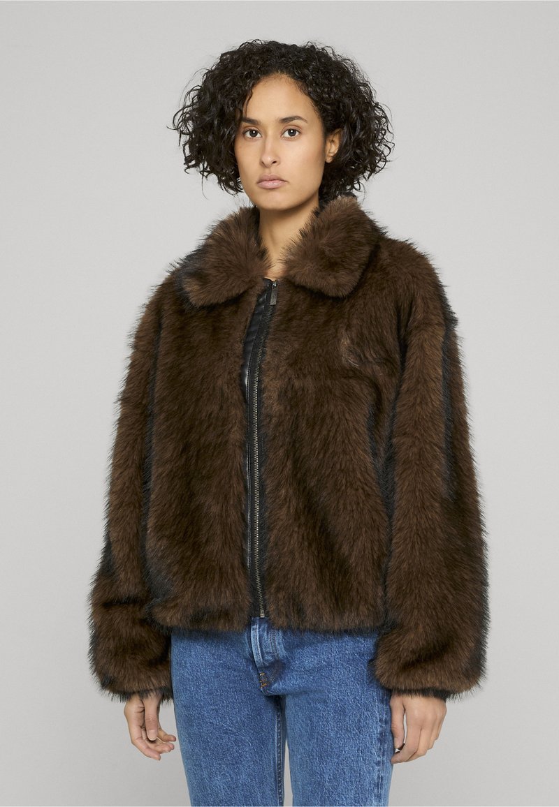 Brown faux fur jacket with a black zipper and collar, featuring long sleeves and a boxy cut, worn over blue jeans.