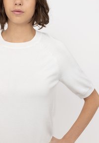 White short-sleeve knit top with a ribbed round neckline and raglan seams. The fabric has a smooth texture, ensuring a fitted silhouette.