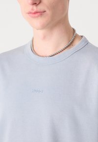 Lyseblå bomulds t-shirt med runde hals; har et subtilt HUGO logo prentet på brystet. Inkluderer en sølv perlekæde.