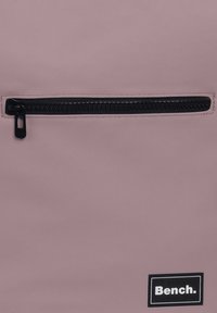 Sac à dos violet avec une finition texturée, doté d'une poche zippée noire et d'un logo "Bench." blanc sur un patch noir.