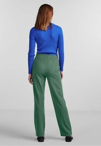 Zielone spodnie z elastycznym pasem i prostymi nogawkami, zestawione z niebieską, prążkowaną bluzką z długim rękawem, widziane z tyłu na neutralnym tle.