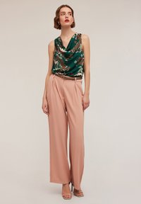 Zielona bluzka z dekoltem w cowl w kwiatowy wzór, zestawiona z szerokimi spodniami w odcieniu różowego piasku i brązowym paskiem. Sandały na wysokim obcasie z odkrytymi palcami.