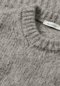 Suéter gris de punto con textura acanalada. Presenta un cuello alto y una etiqueta de tela con el nombre de la marca "hessnatur."