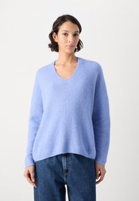 Lichtblauwe v-hals trui van zachte, gestructureerde stof met losse mouwen, gecombineerd met hoge taille donkere spijkerbroek.