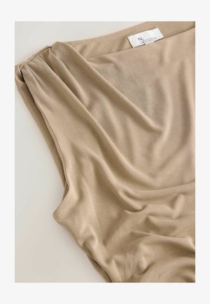 Tissu beige avec un drapé doux et une texture lisse, avec une étiquette visible sur le bord supérieur indiquant la marque ou la collection.