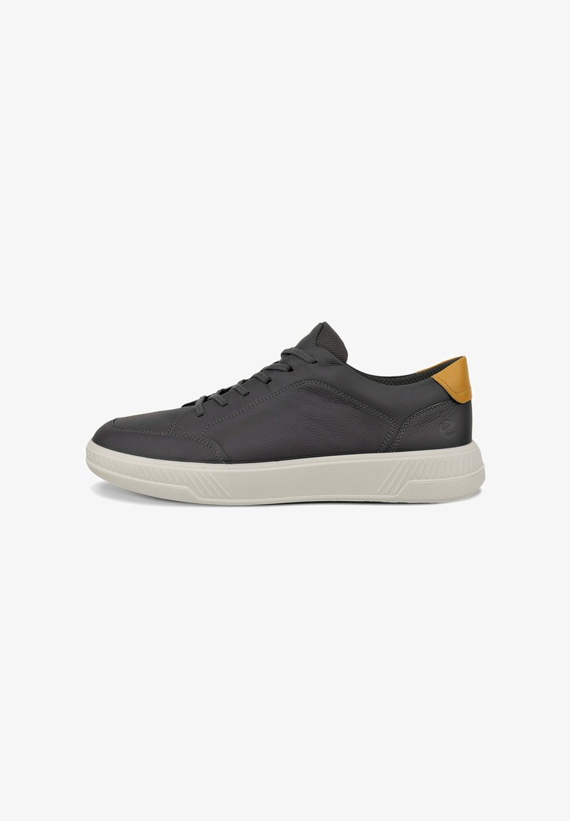 Mörkgrå lädersneakers med vit gummisula, snördesign och tanfärgad accent vid hälen. Har en slät textur och minimalistisk stil.