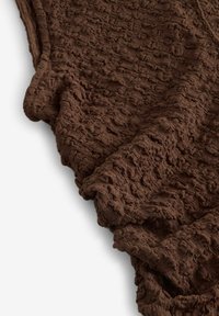 Brūna teksturēta auduma ar viļņainu, krunkainu rakstu, kas sastāv no mīkstām, neregulārām virsmām un bagātīgas, zemes krāsas.