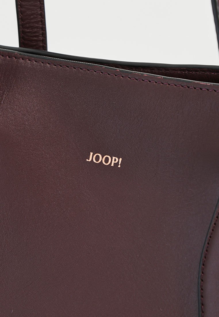 Dunkelbraune Lederhandtasche mit sichtbaren Nähten und goldenem JOOP!-Logo, das zentral am oberen Rand platziert ist.