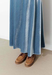 Jupe longue et scintillante de couleur bleue, avec une texture lisse, associée à des chaussures en suède marron avec des lacets rouges et une semelle robuste.