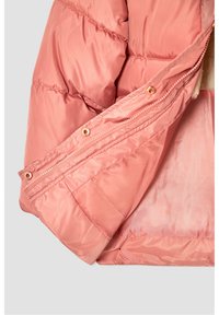 Ocieplana kurtka w kolorze brzoskwiniowym, wykonana z gładkiego, błyszczącego materiału, z zamkiem błyskawicznym i widocznym przeszyciem. Wnętrze wyłożone miękkim, jasnym materiałem.