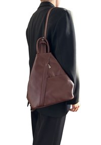 Zaino in pelle marrone dalla forma triangolare, con una tasca frontale, doppio manico superiore e una tracolla singola. Texture liscia.