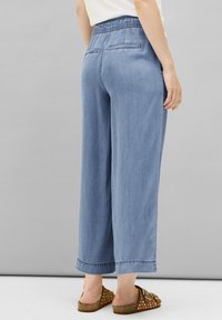 Jasnoniebieskie, szerokie dżinsy z elastycznym paskiem, dwoma tylnymi kieszeniami i wyszywanymi detalami na końcu, w połączeniu z brązowymi klapkami w kropki.