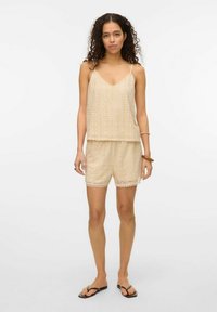 Beige hækle-sæt med en v-udskæring tanktop og matchende shorts med bølget kant. Stoffet har et tekstureret blondermønster.