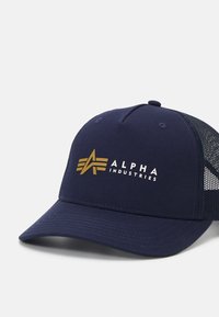 Temno modra bejzbol kapa z ojačanim vizorjem, mrežasto hrbtno stranjo in zlatim logotipom z napisom "ALPHA INDUSTRIES" ter zvezdnimi akcenti.