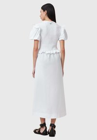 Witte jurk met een geschulpt lijfje, korte puffmouwen, een gerimpelde zoom en een lange rok. Gecombineerd met zwarte sandalen.