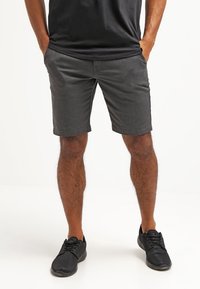 Shorts gris en tissu léger, avec un devant plat et deux poches latérales, associés à des chaussures de sport noires.